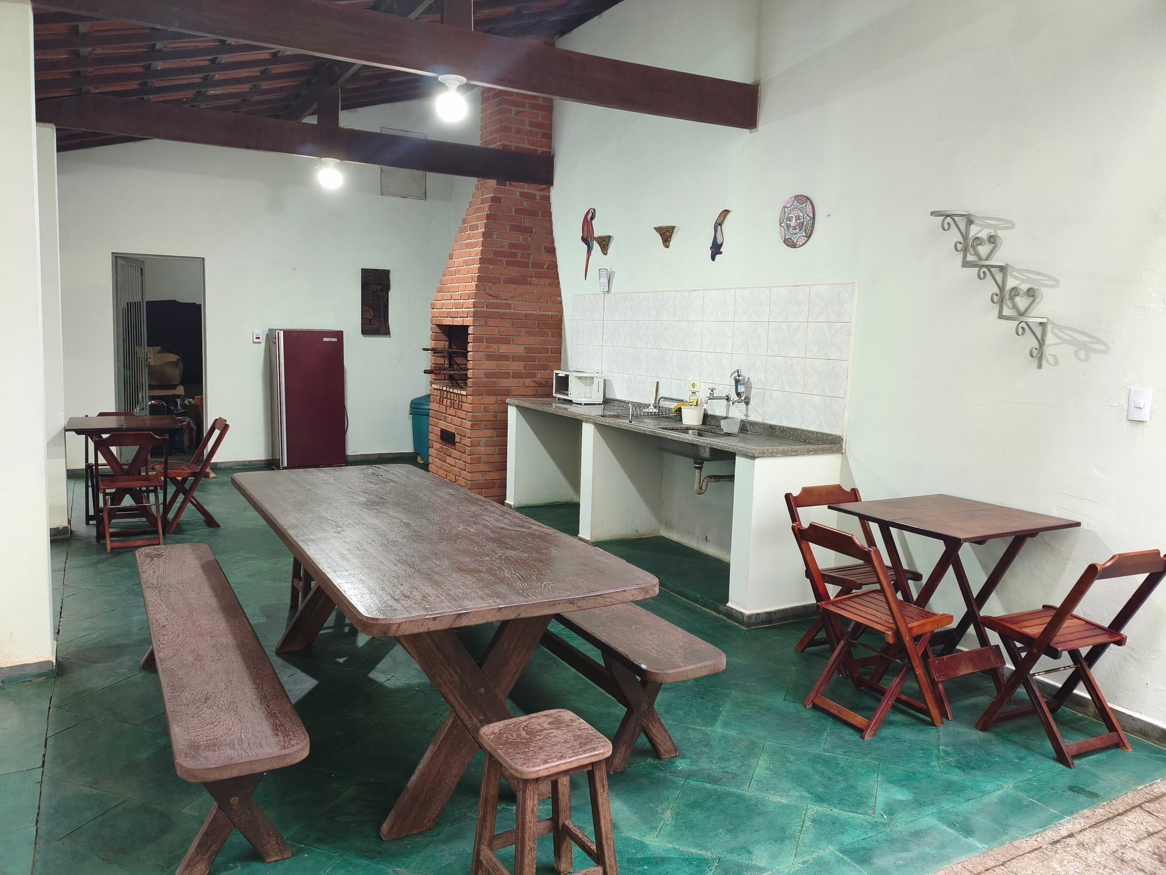 A área gourmet por dentro: mesa grande com bancos, churrasqueira de tijolo e bancada