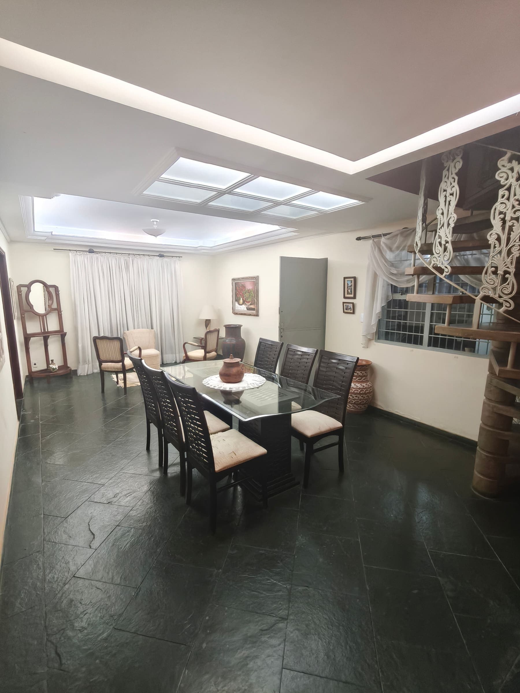 Sala de jantar com mesa de vidro para oito, poltronas e escada caracol ao fundo