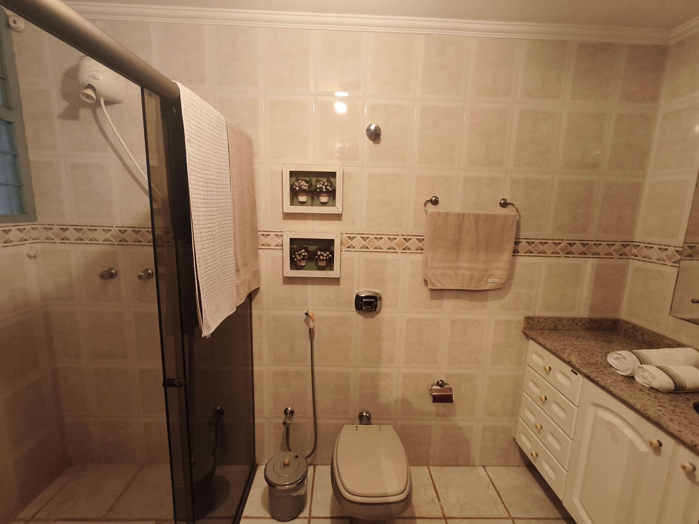 Banheiro de suíte com box de vidro, toalhas e revestimento claro